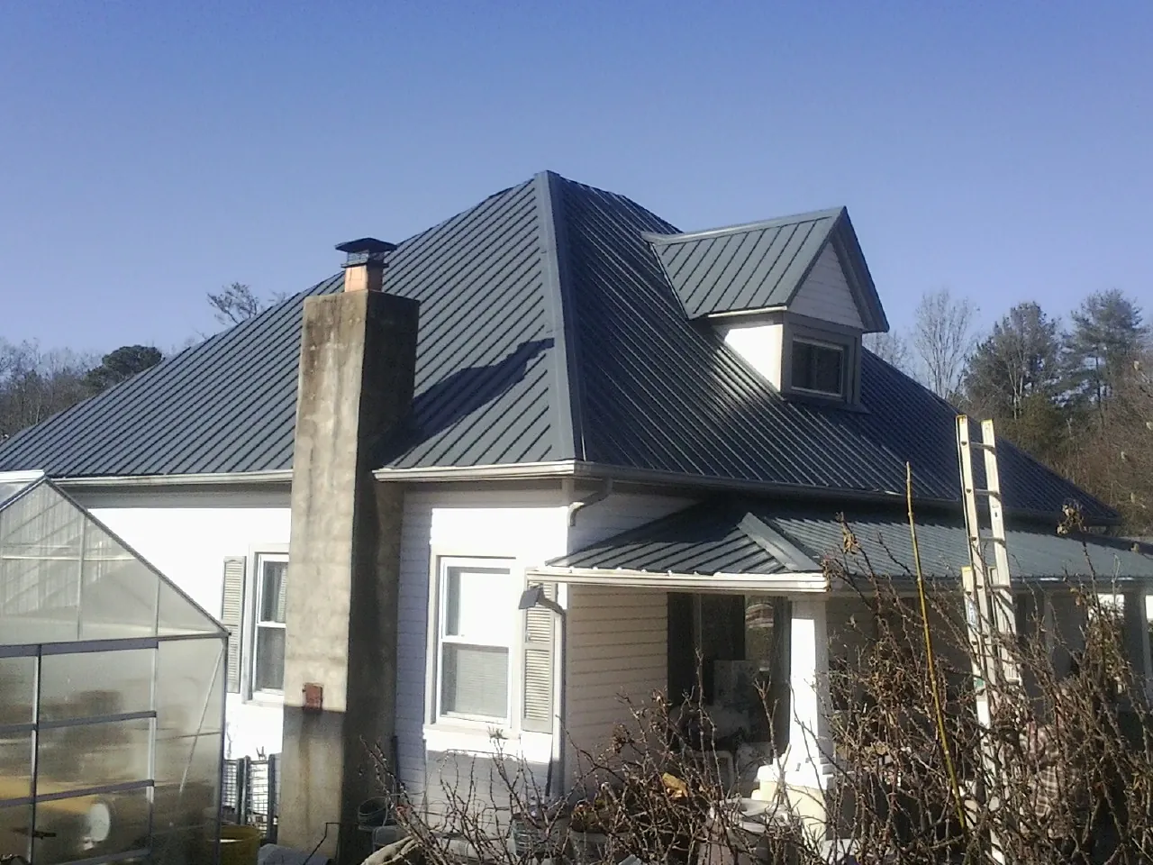 Dark blue standing seam metal roof on a white farmhouse with dormer — Slate & Tile Roof Repair by Roofing Brothers in Ute