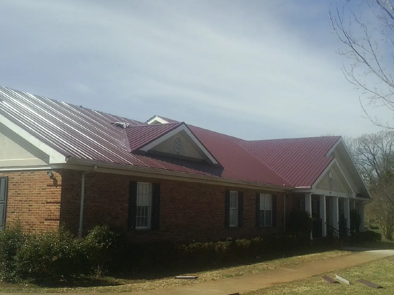 Red metal roof with gabled entries on a long brick building, from a Hail Damage Roof Repair job in Ute