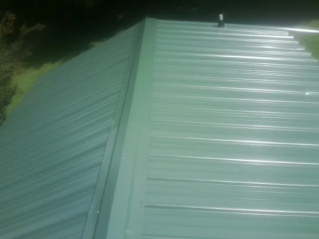 New green metal panels meeting at the ridge of a roof — Flat Roof Repair work by our crew in Ute