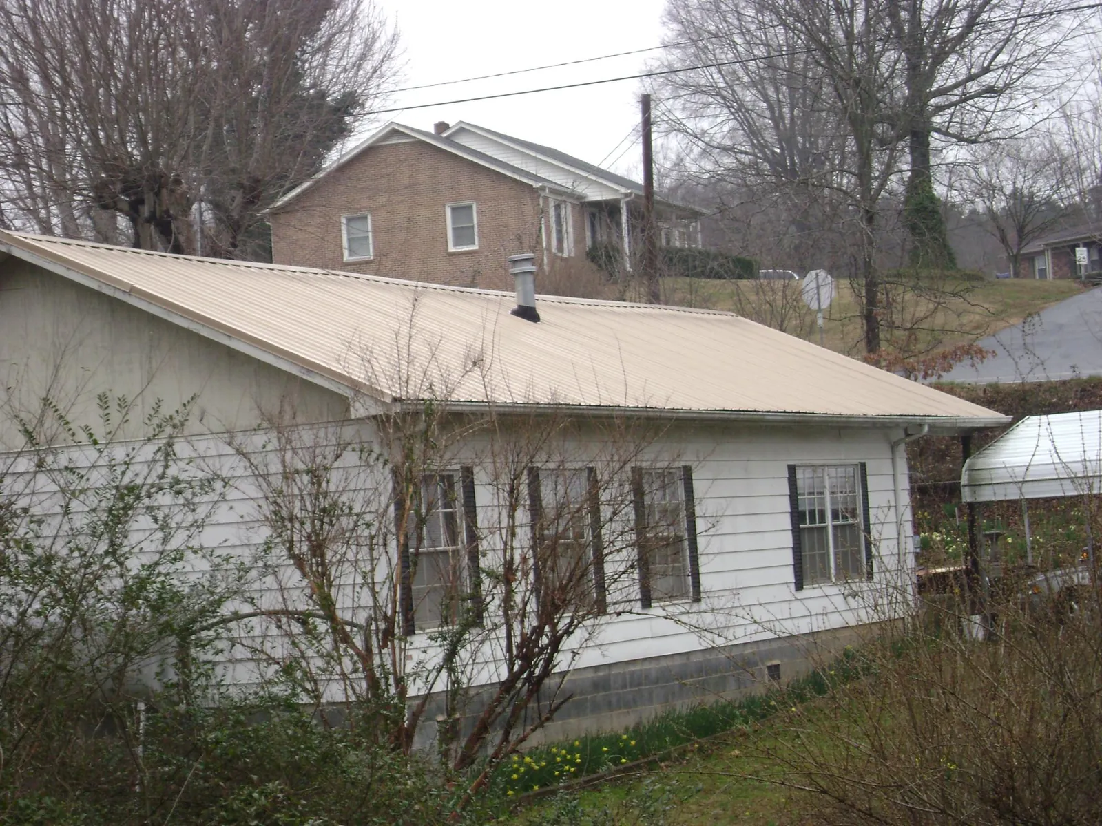 Tan metal roof on a white sided house set into a hillside — Commercial Roofing by Roofing Brothers in Ute