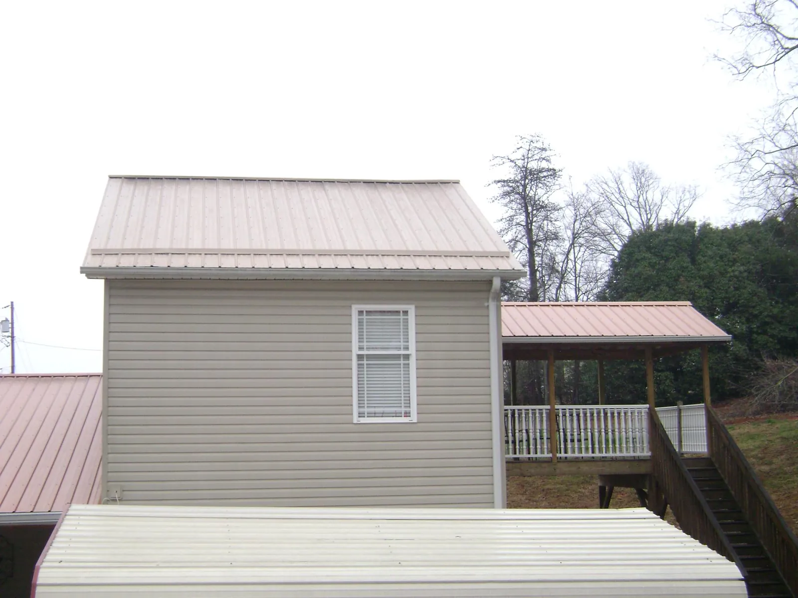 Tan metal roofs on a two story addition and attached porch, from a Roof Replacement job in Ute